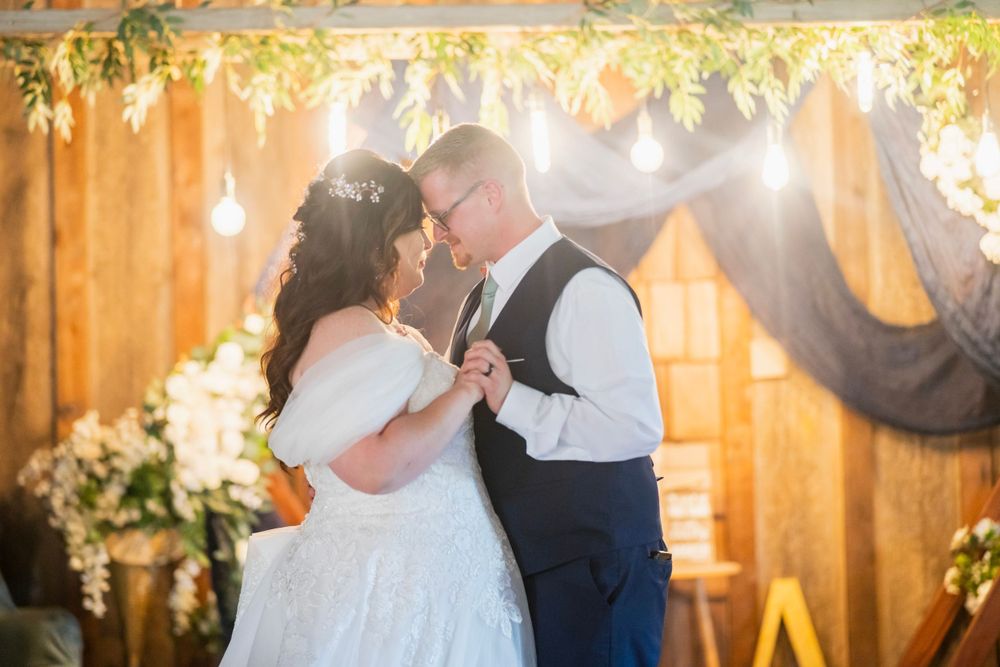 Bride and groom sharing an intimate first dance under string lights in a decorated barn venue.