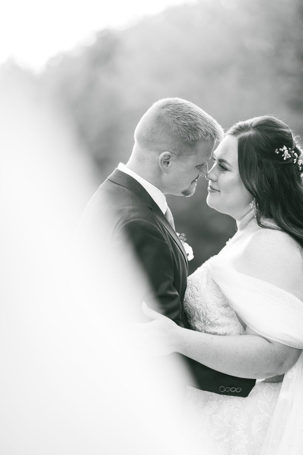 Black and white portrait of bride and groom touching foreheads tenderly on their wedding day.