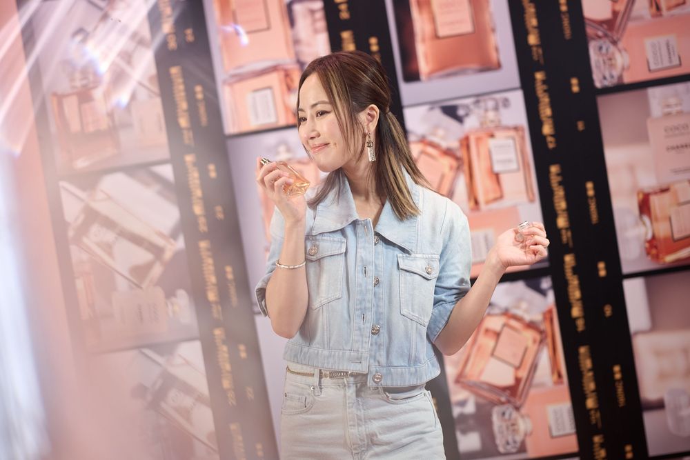 Young Asian woman in denim jacket and skirt smelling perfume in a luxury fragrance store.