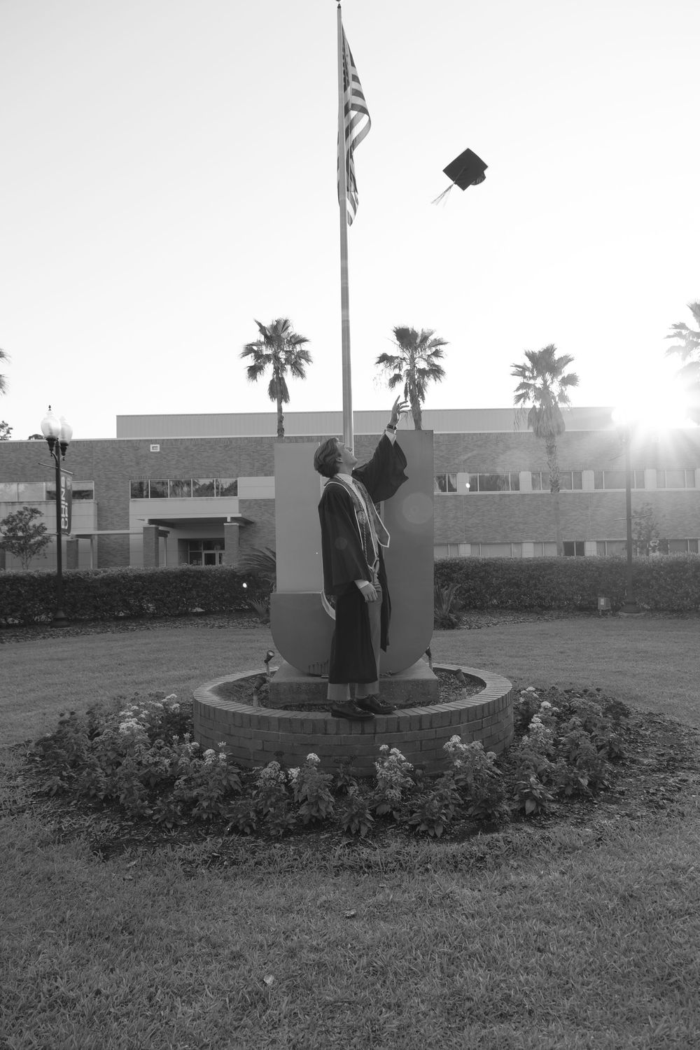 Black and white silhouette of graduate tossing cap beside flagpole at Jacksonville University campus.