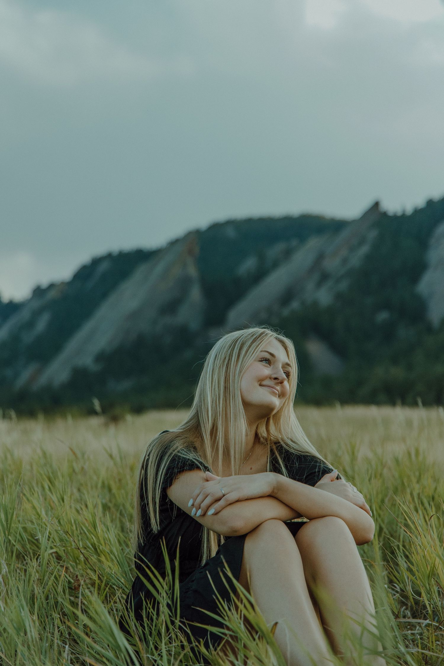 high school aged girl facing to the right in a grass field with mountains behind her