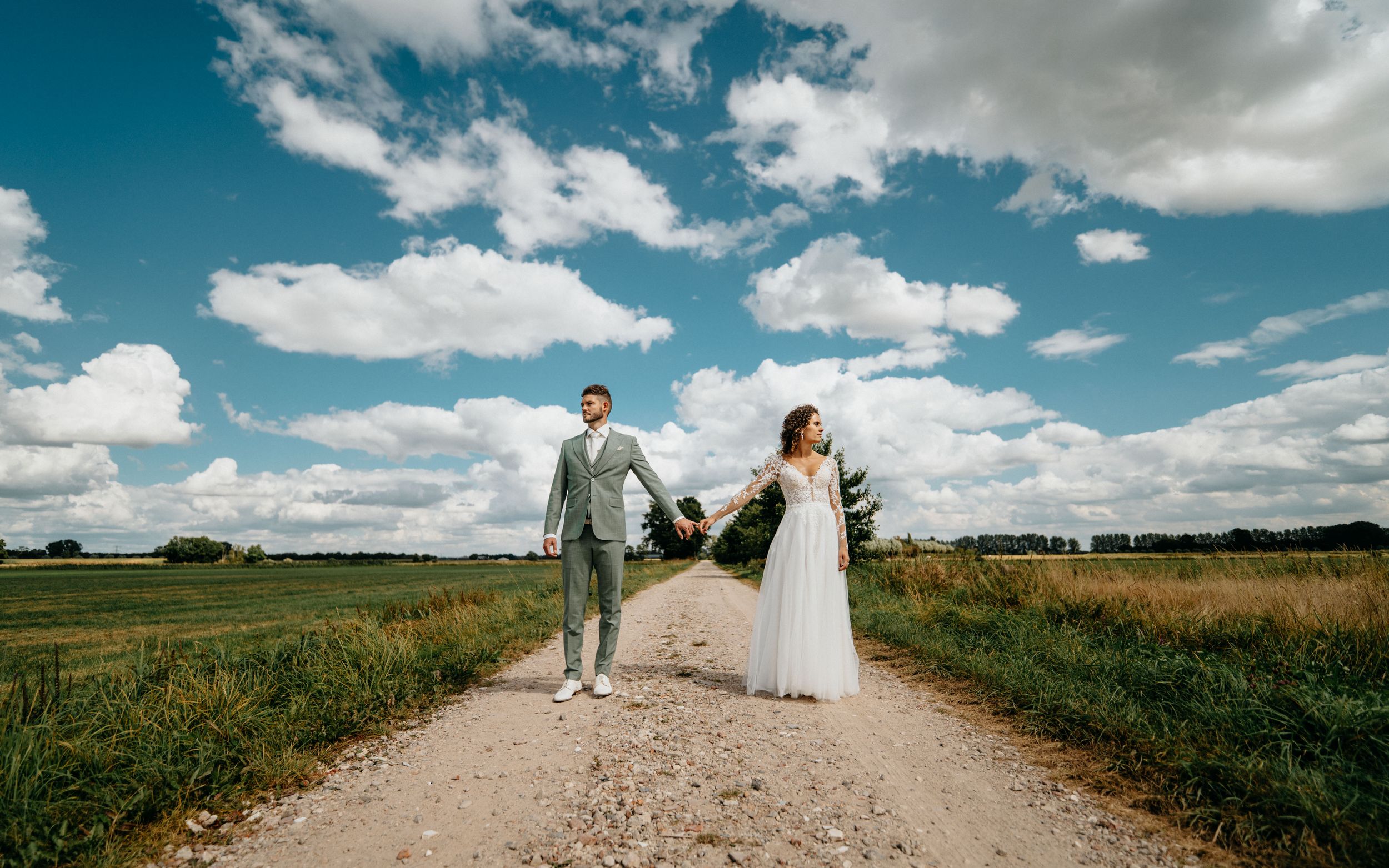 Een statig portret van een bruidspaar onder de blauwe lucht met stapelwolken, zoals de Hollandse Meesters deze zouden afbeelden.