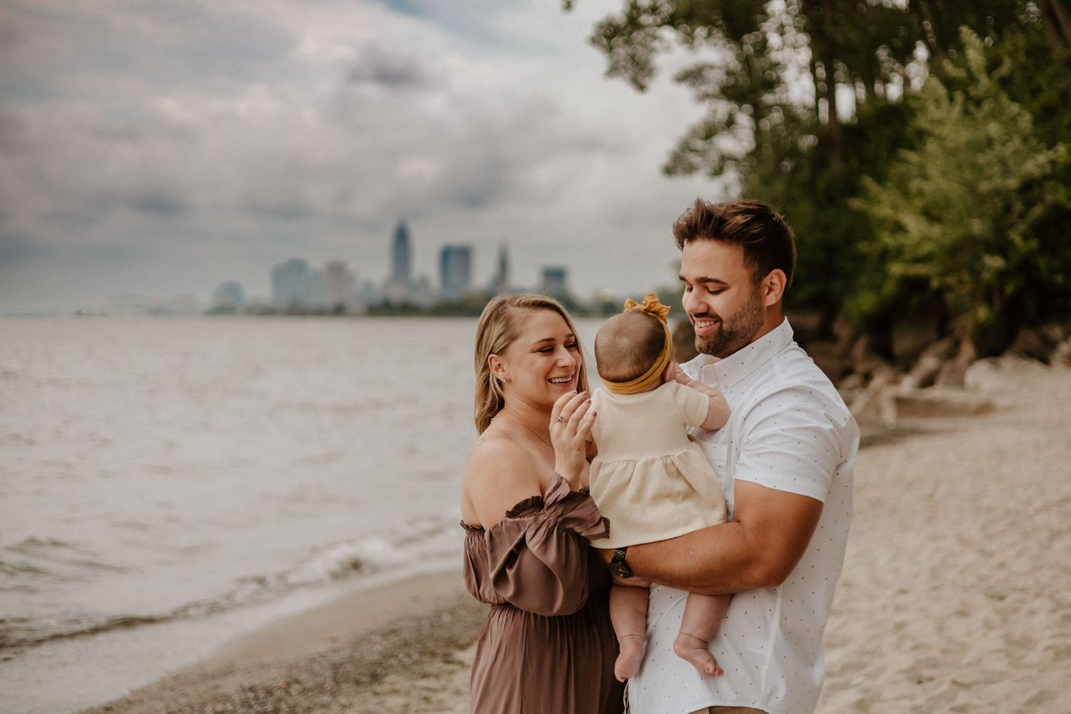 A family shares a tender moment on the beach with a city skyline visible in the background.