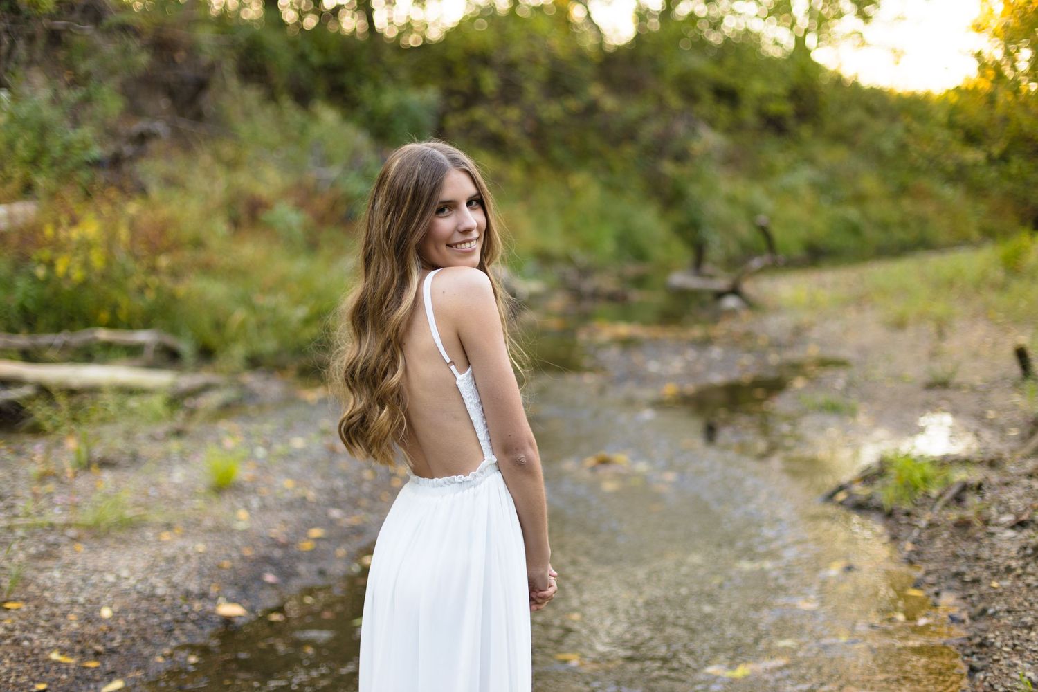 A mid-length portrait of a girl wearing a white summer dress, posing in front of a creek bank outside of Neoga, Illinois.