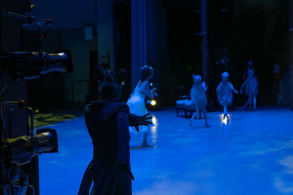 Silhouetted performers stand on a stage illuminated by blue lighting during a theatrical production.