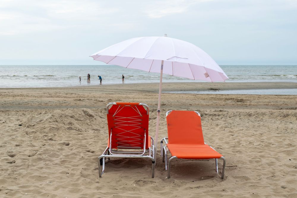 Two beach chairs under pink umbrella on empty sandy beach.