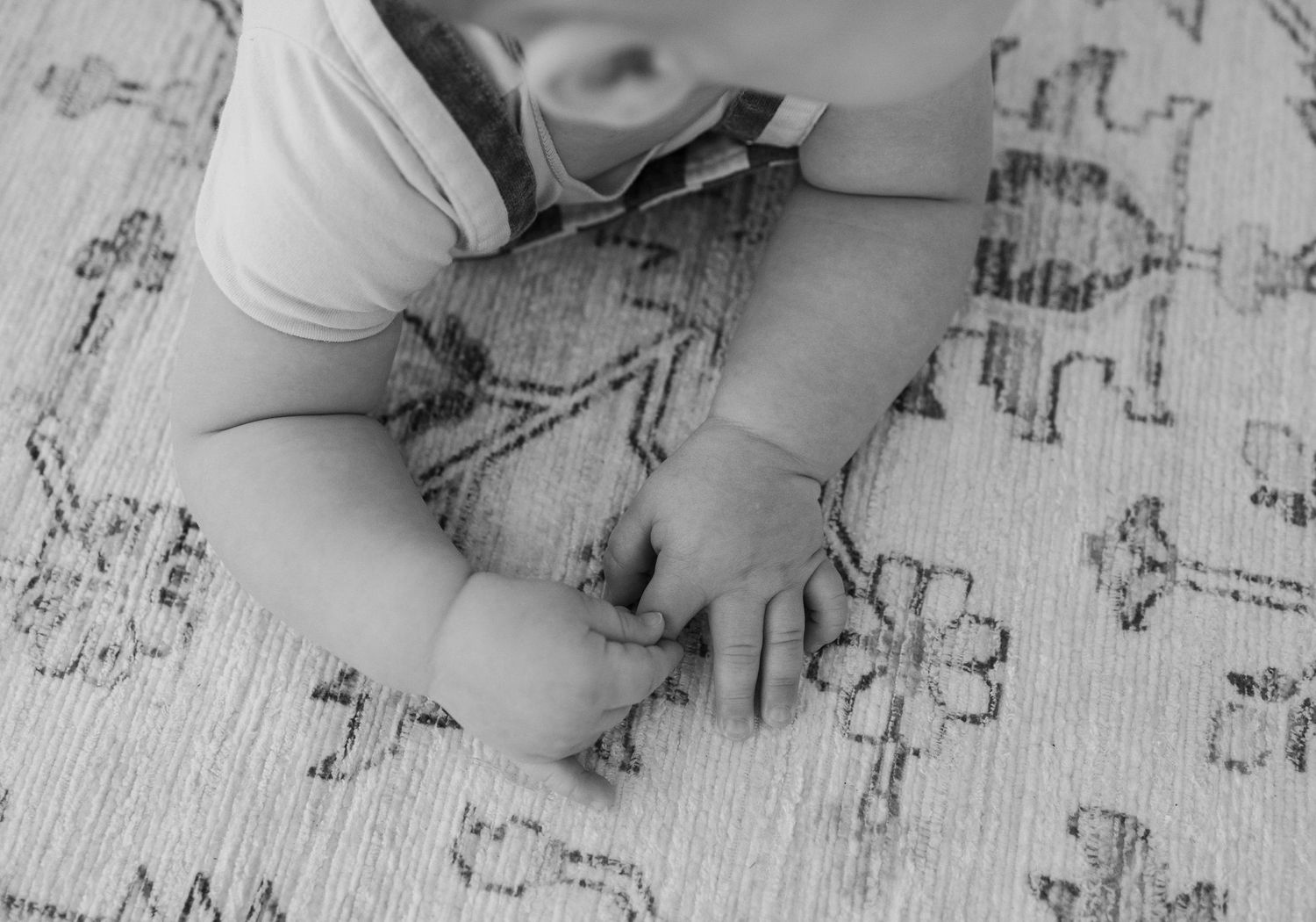 Small child's hands draw on a patterned surface with marker in black and white photo.
