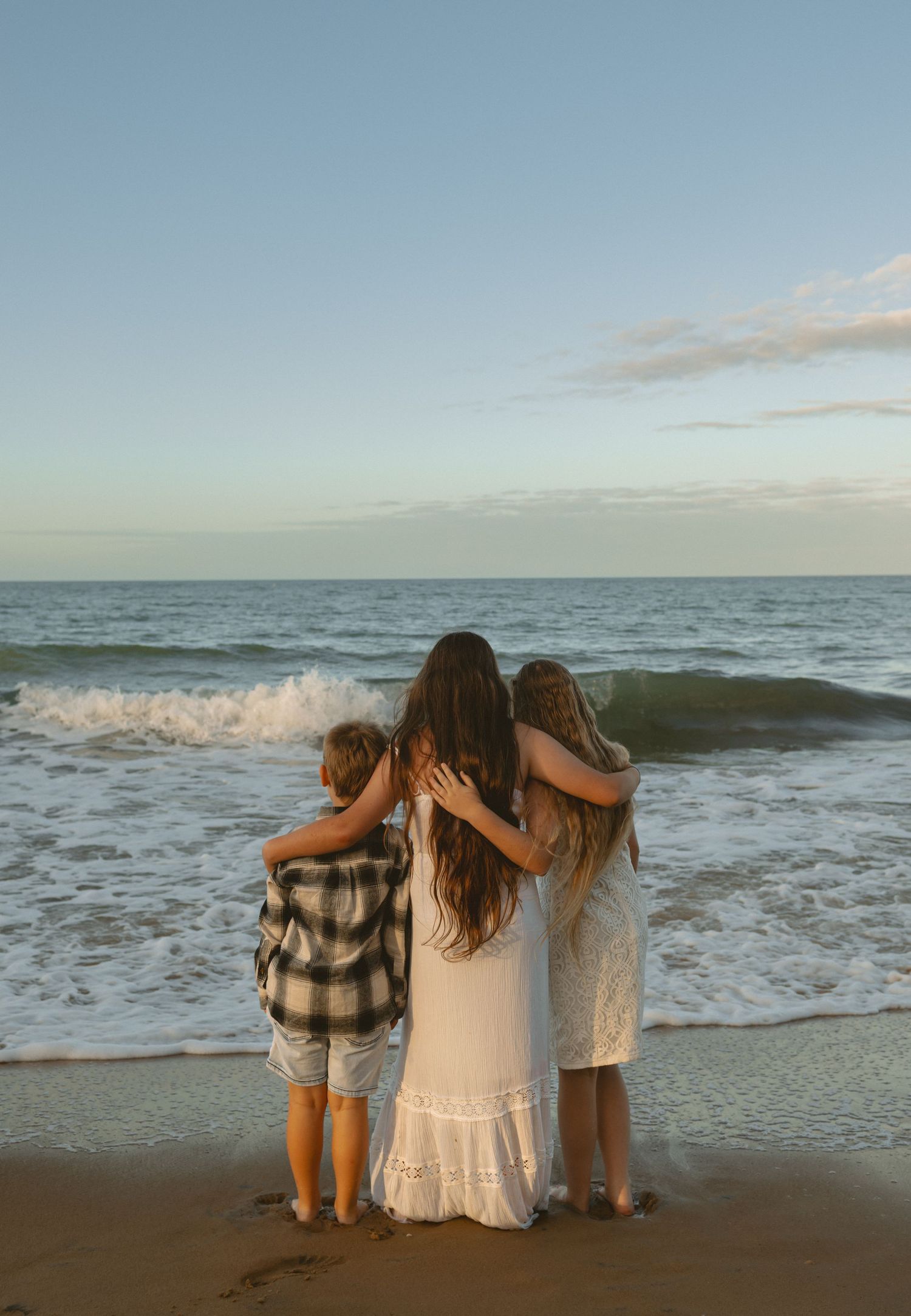 Friends huddled together on a sandy beach at sunset watching the ocean waves roll in.