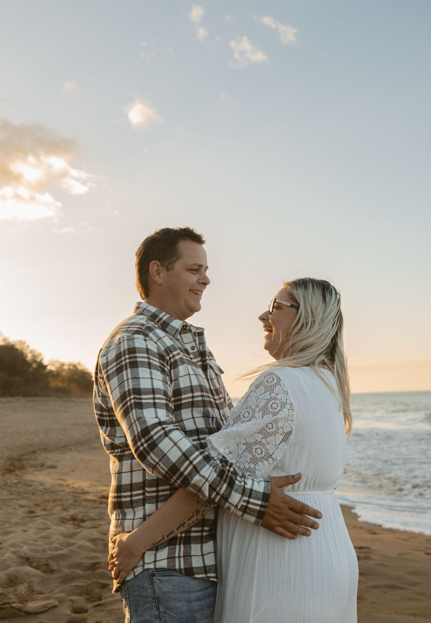 A romantic couple shares a joyful moment together on the beach at sunset, dressed in casual attire.