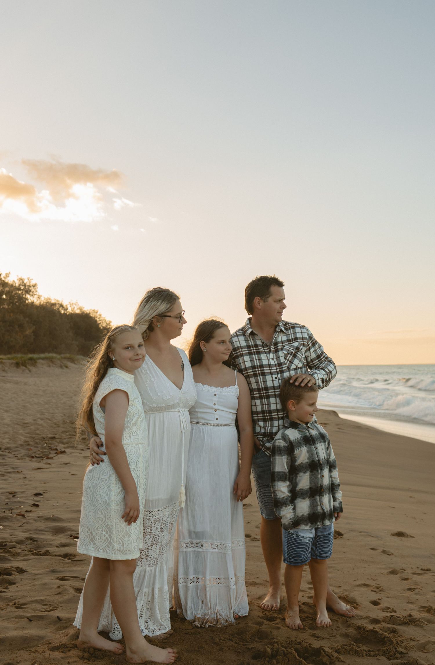 A group stands together on a sandy beach at sunset wearing white dresses and casual attire.