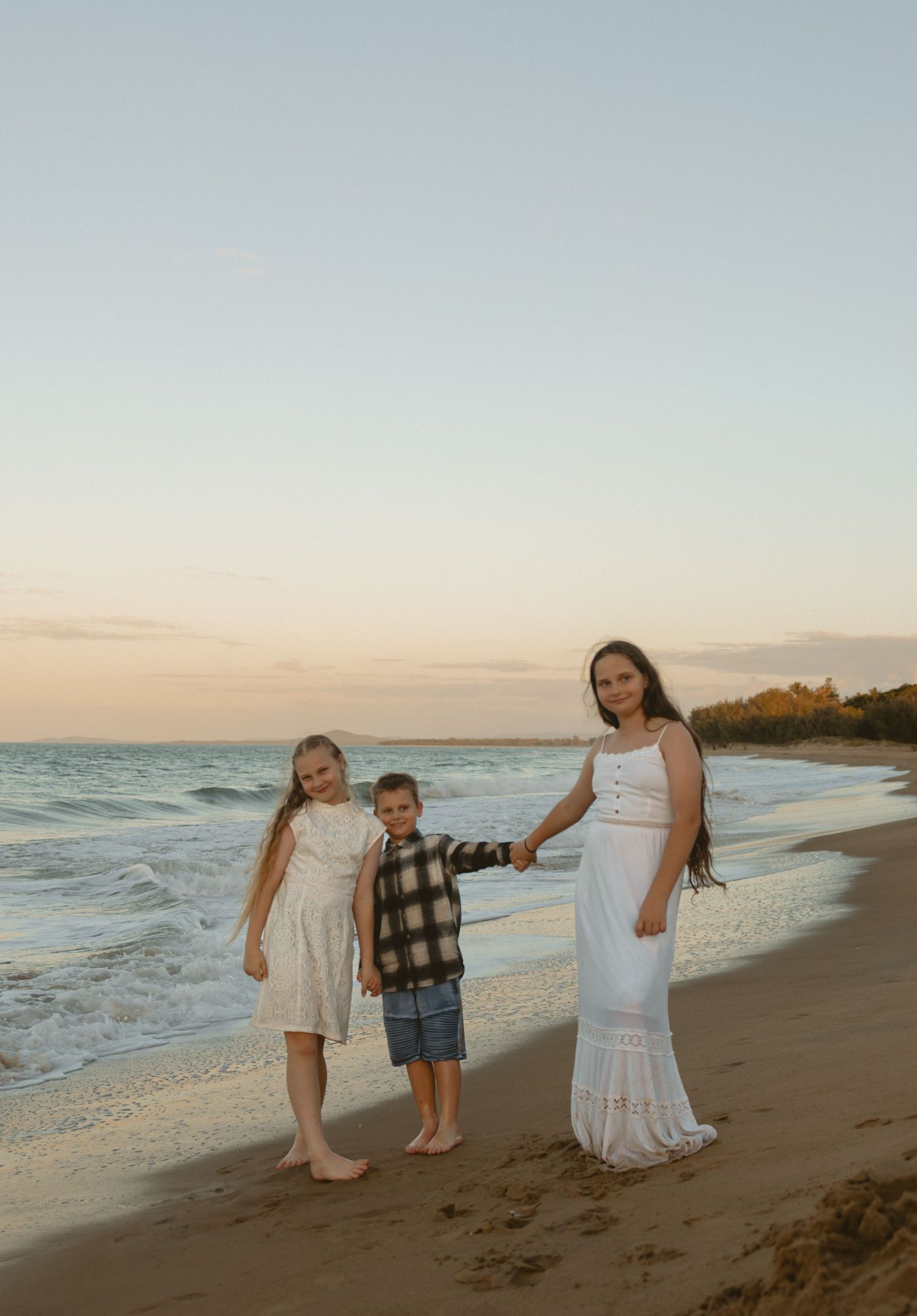 Three people enjoy a warm sunset walk along a peaceful ocean beach with waves gently rolling in.