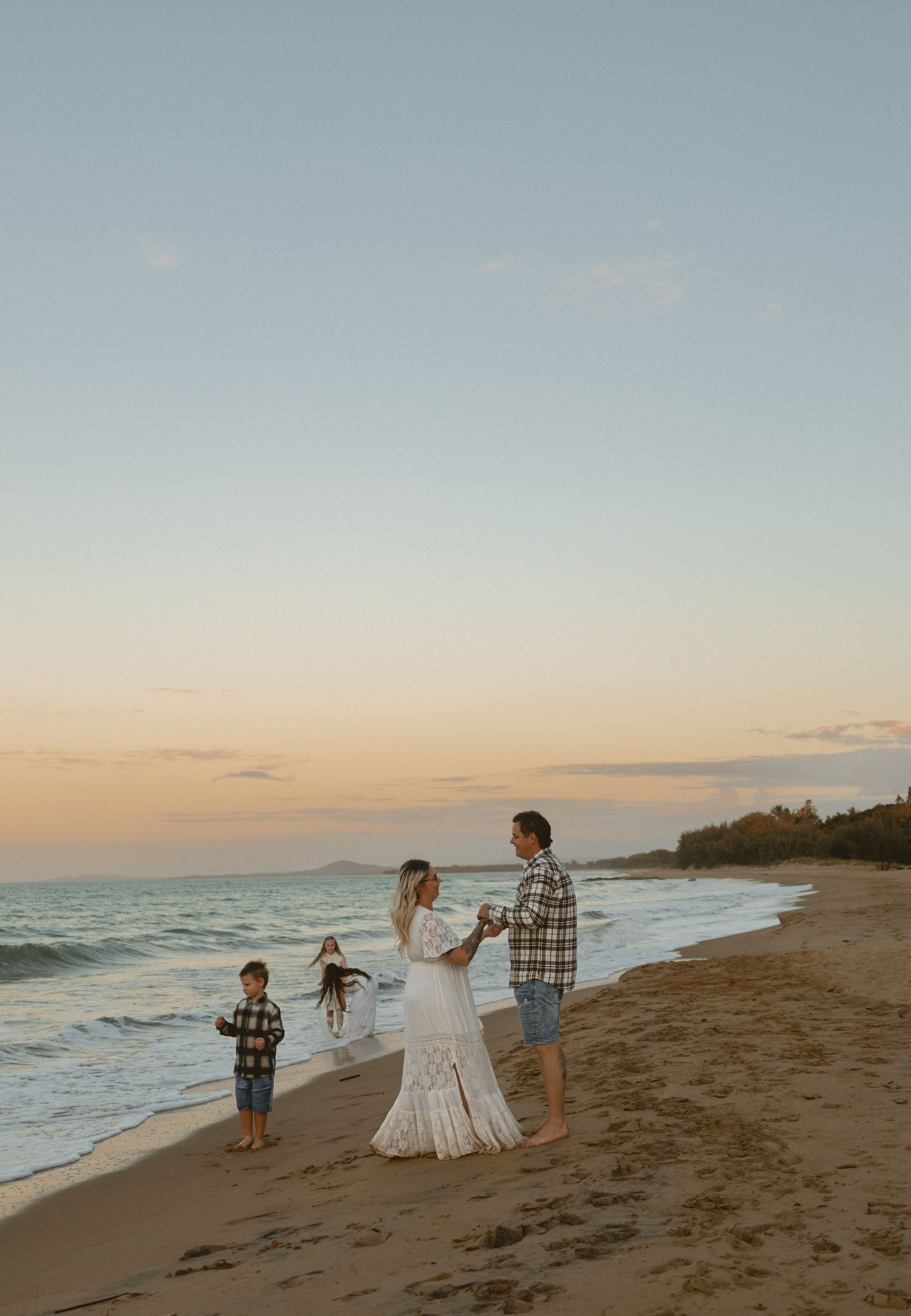 Family enjoying a sunset moment together on a beautiful sandy beach with waves rolling in at golden hour.