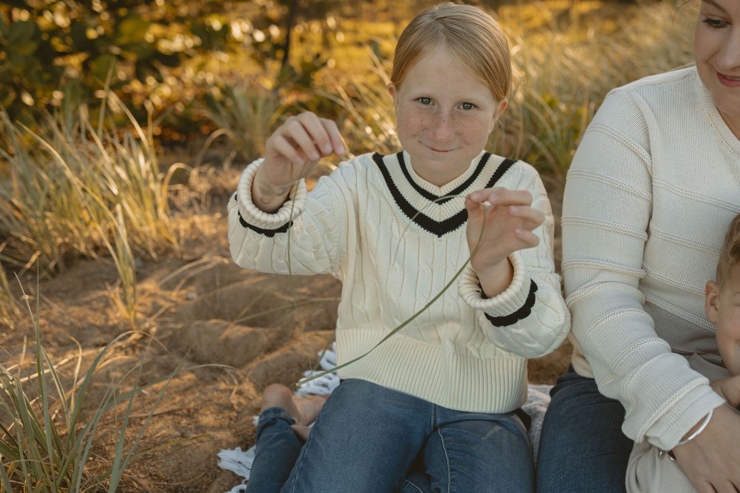 Family wearing cream colored sweaters poses together during golden hour in an outdoor autumn setting.