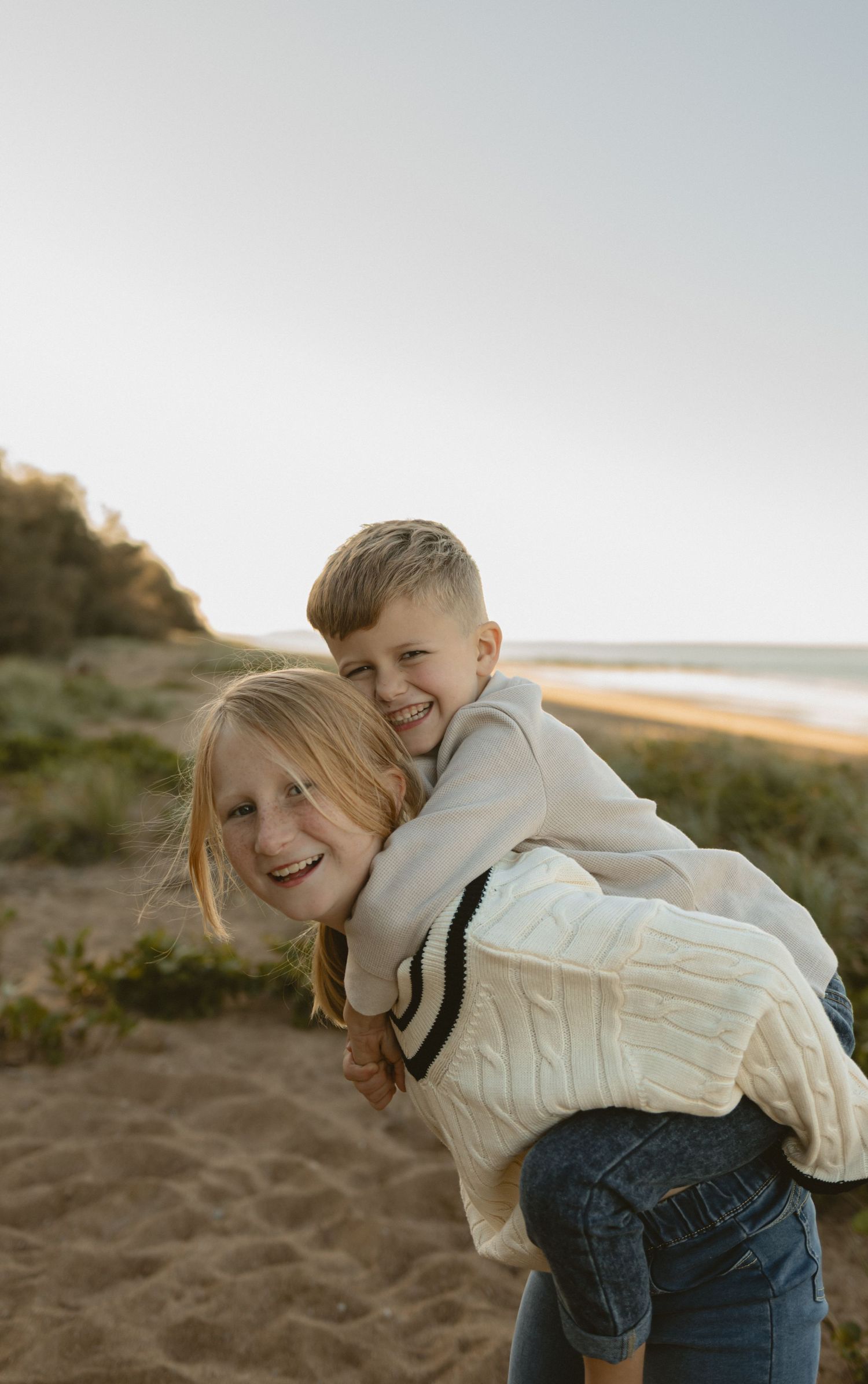 A joyful candid moment captured between two people embracing and smiling playfully on a sandy beach at sunset.