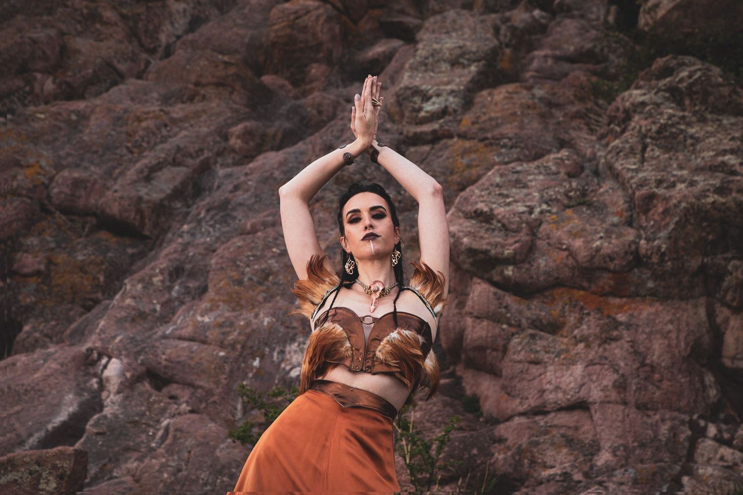 Artistic dance pose in brown leather costume against rocky canyon wall.