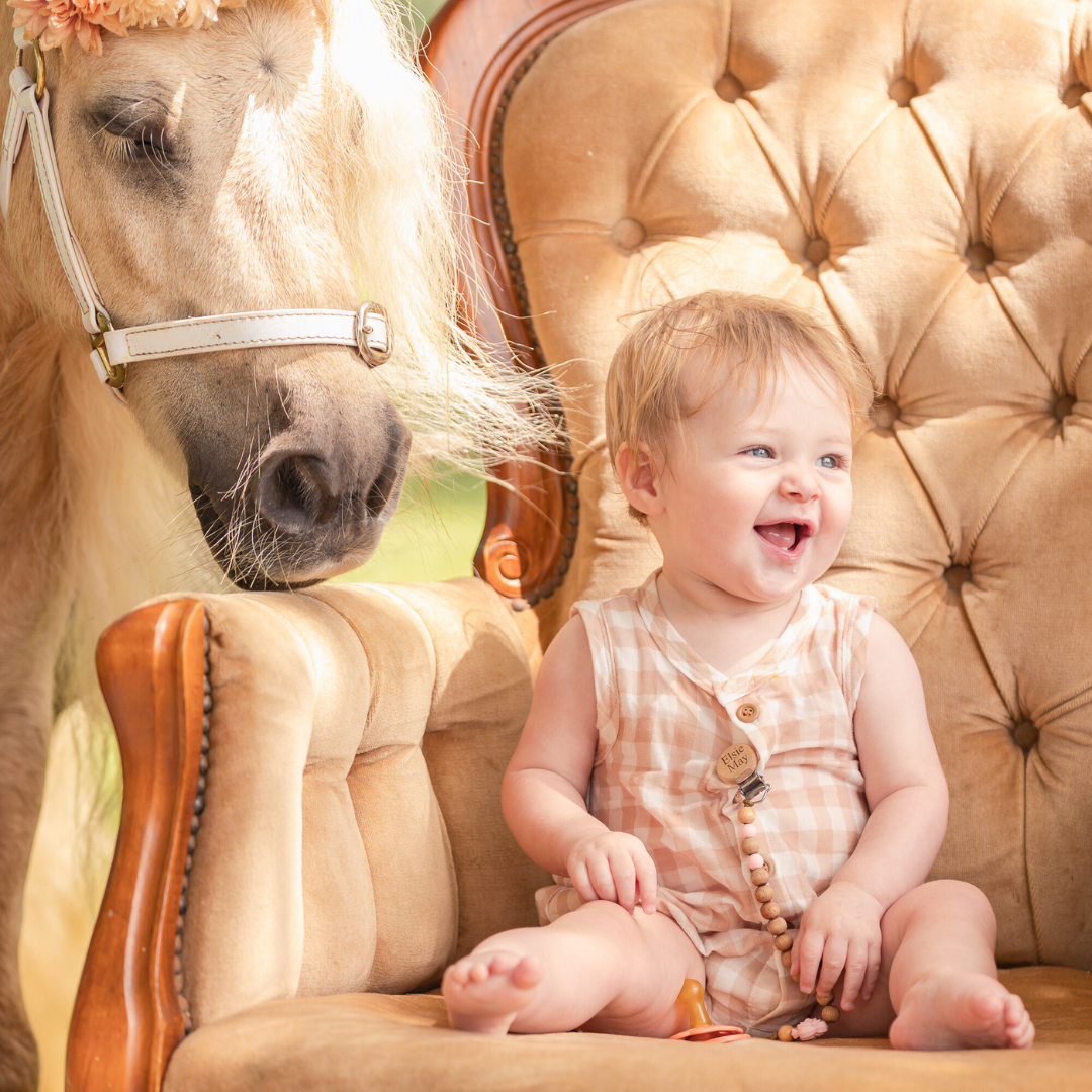 A joyful moment captured on a tufted beige chair with a horse nearby. One Year Old Birthday Party Photoshoot.