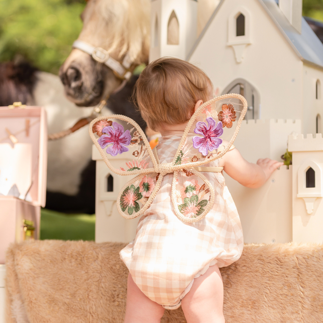 A dreamy scene with butterfly wings, a white castle, and a horse in soft lighting. One Year Old Birthday Party Photoshoot.