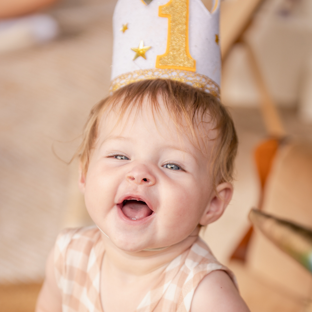 One Year Old Birthday Party Photoshoot. Gold glitter crown and party decorations sparkle in celebration setting.