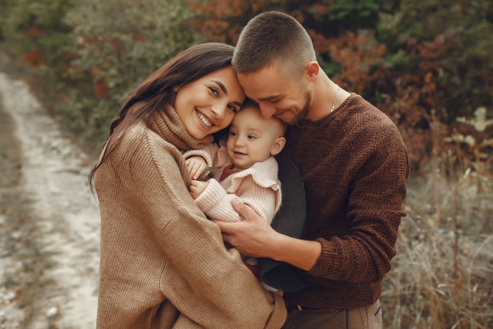 Cozy family portrait outdoors with couple and baby wearing brown sweaters.