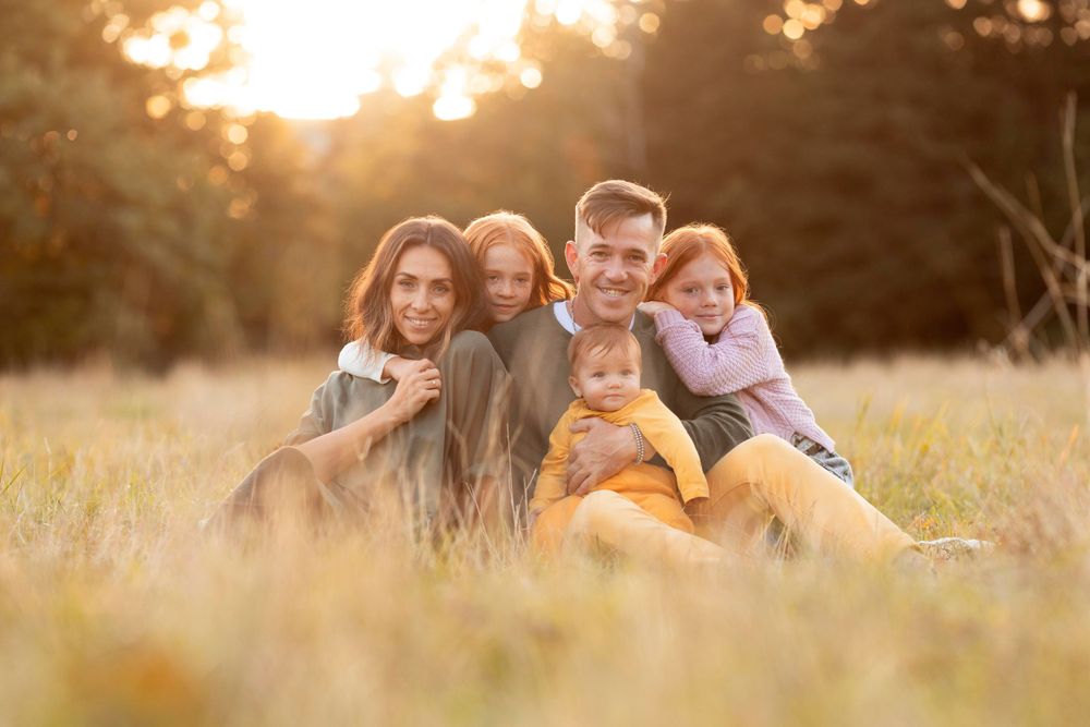 A loving family sits together in a sun-drenched meadow during golden hour while wearing casual attire.
