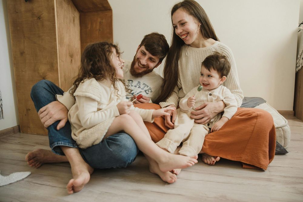 Candid family moment with parents and children laughing together on wooden floor.