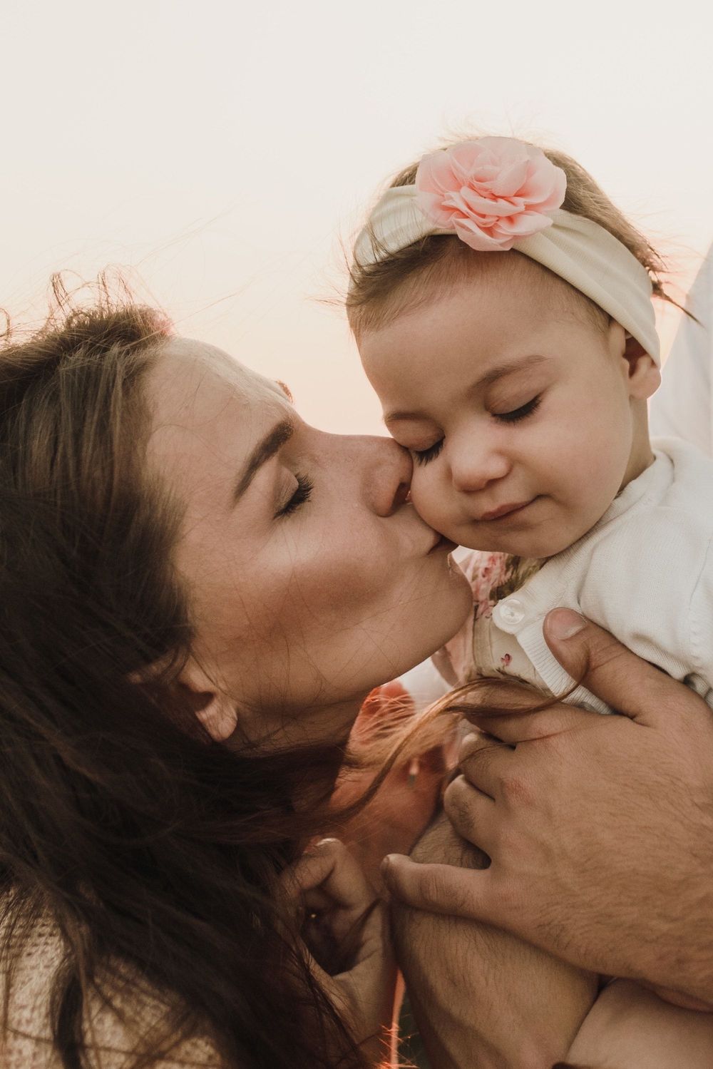A tender moment between parent and baby with a pink floral headband in warm lighting.