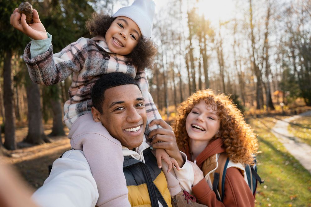 A joyful family moment captured outdoors in a park during autumn with sunlight streaming through the trees.