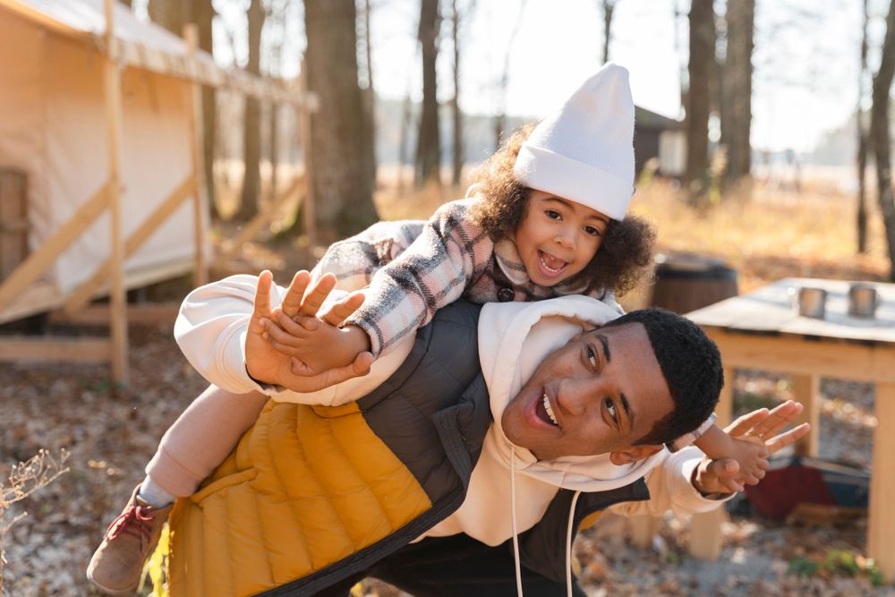 Two individuals in aprons and chefs hats pose playfully outdoors during an autumn day in the woods.