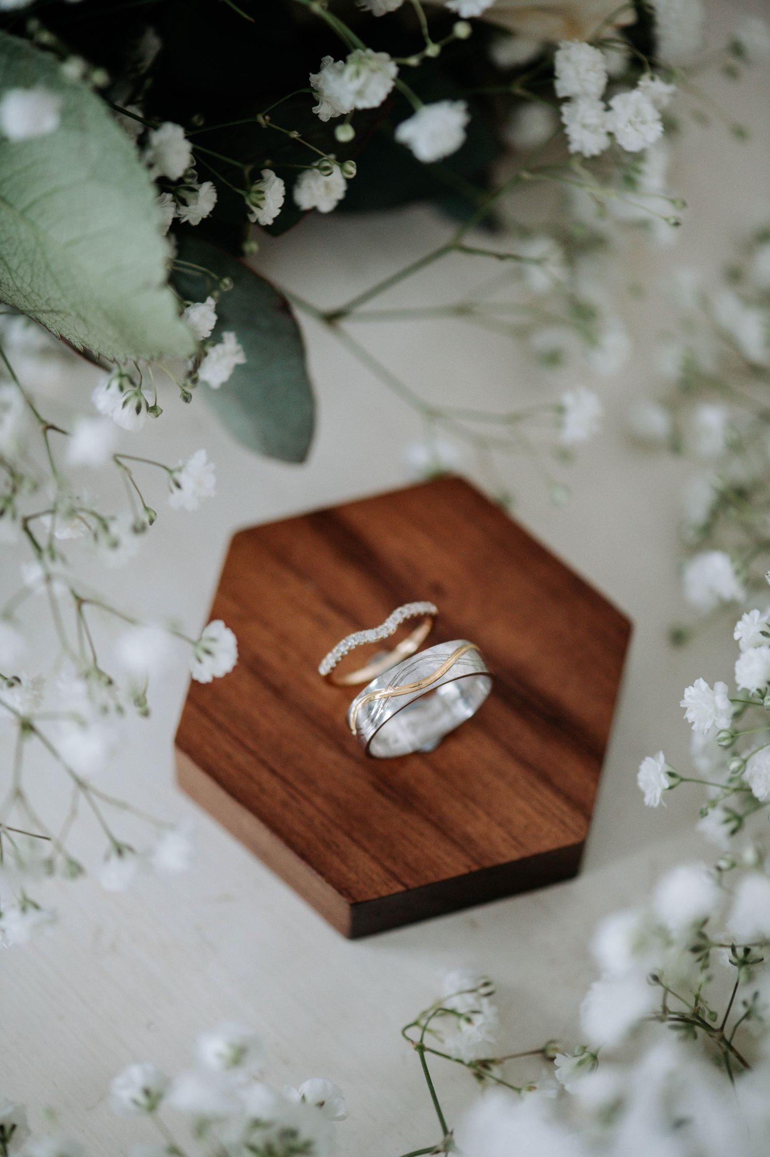 Wedding rings displayed on wooden hexagon with delicate baby's breath flowers.