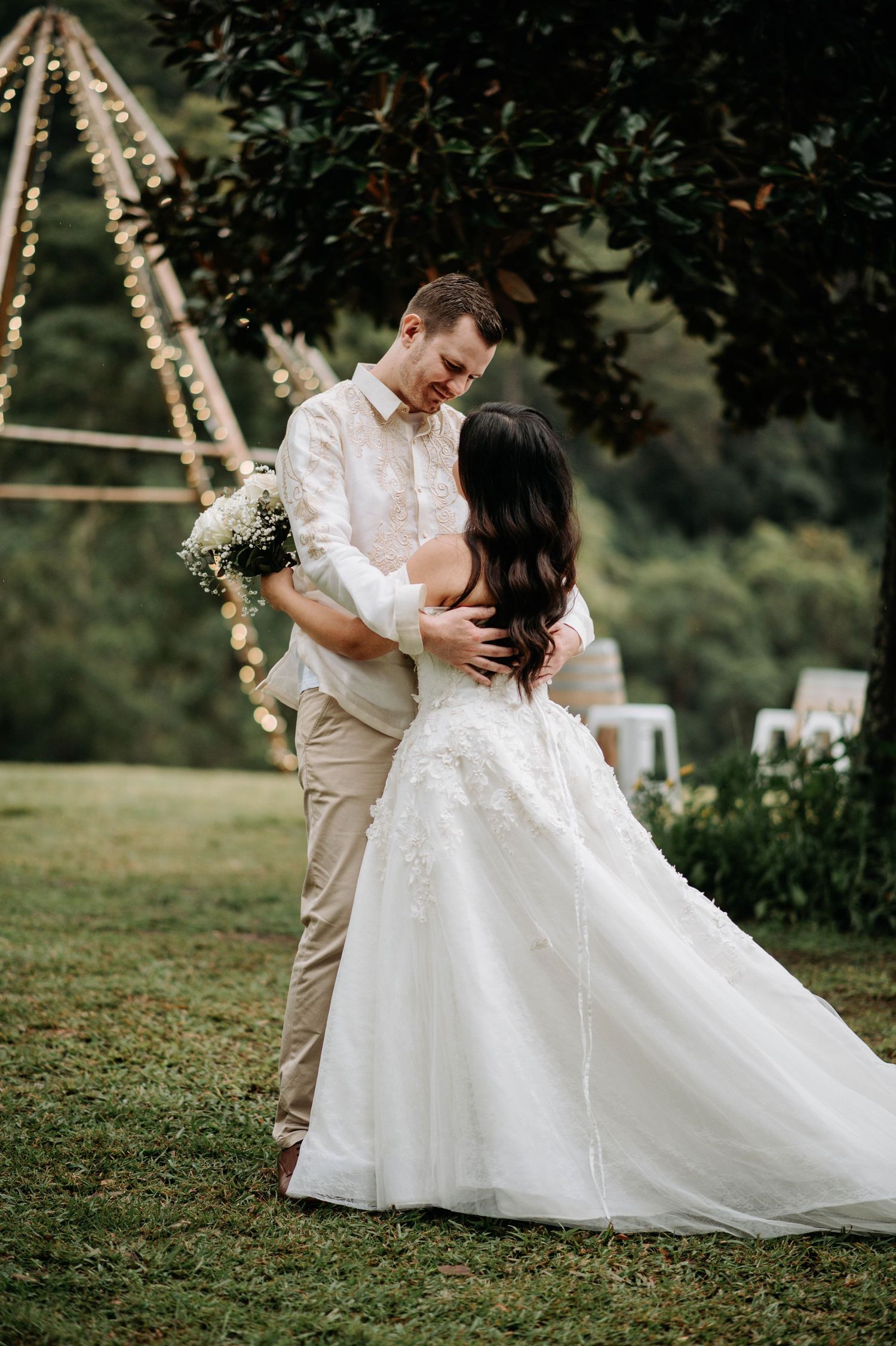 A romantic wedding couple embrace during their outdoor celebration near a decorated teepee structure.