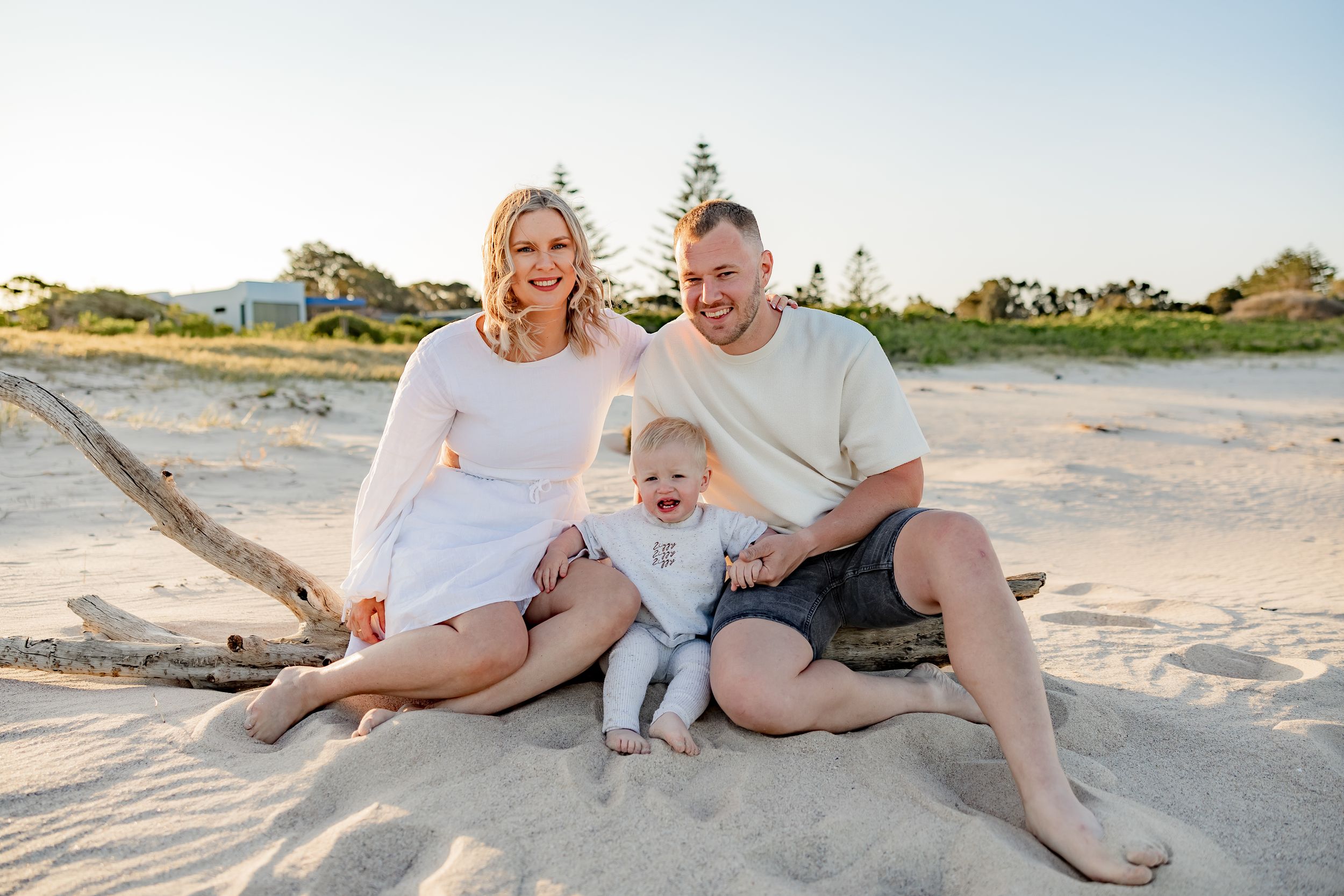 A family shares a candid moment while sitting on a sandy beach during sunset.