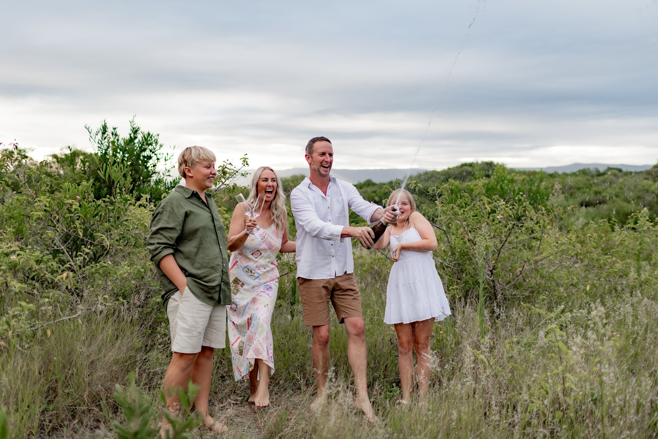 A group poses together laughing in casual attire against a desert landscape.