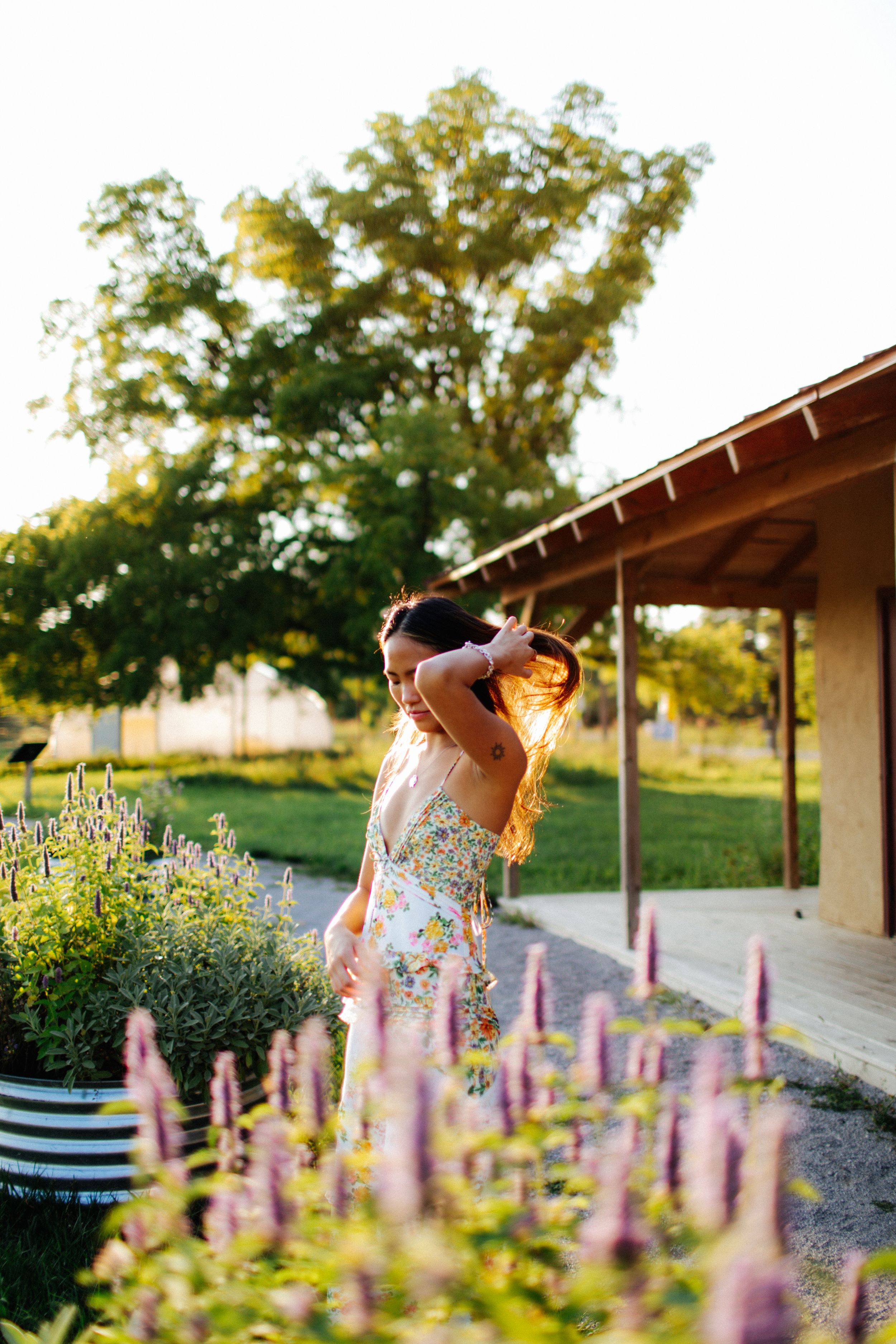 Garden scene with purple flower spikes in foreground and rustic building in background during sunset.