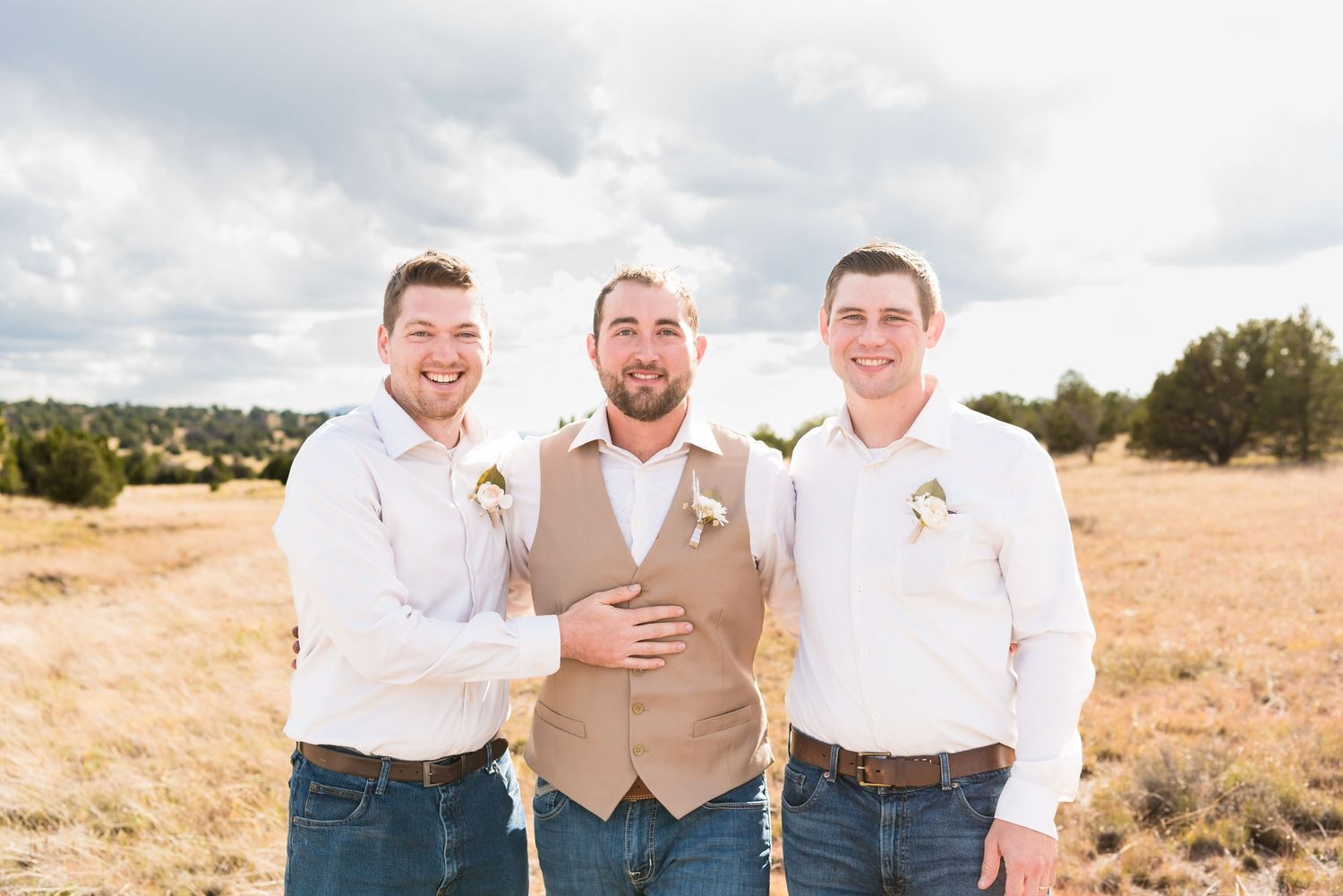Three men in casual western attire pose in a sunlit field.