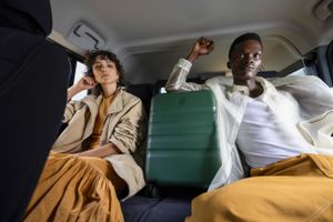 Passengers enjoy a road trip in car backseat with Antler luggage visible.