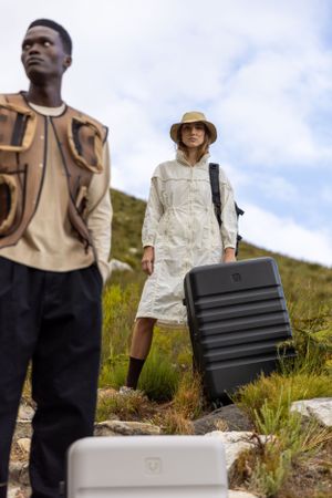Travelers with suitcases posing on rocky mountain trail under cloudy sky.