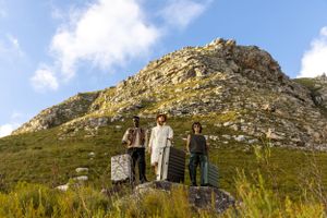 Group of travelers with suitcases posing on a mountainside with rocky cliffs.