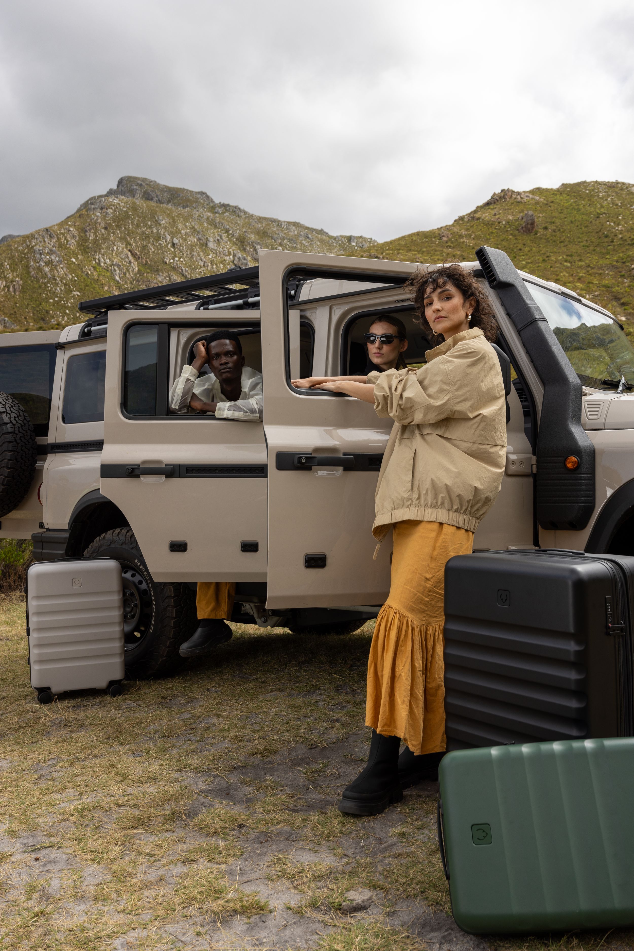 Travelers loading luggage into a silver off-road vehicle in mountainous landscape.