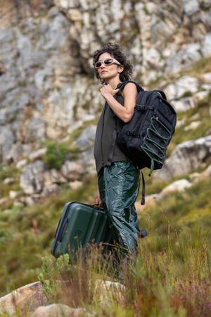 Traveler carrying backpack and luggage while hiking in mountainous terrain.