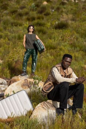 Travelers resting on rocky outcrops in mountainous wilderness with luggage.