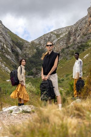 Adventure travelers with backpacks pose on rocky mountain trail.