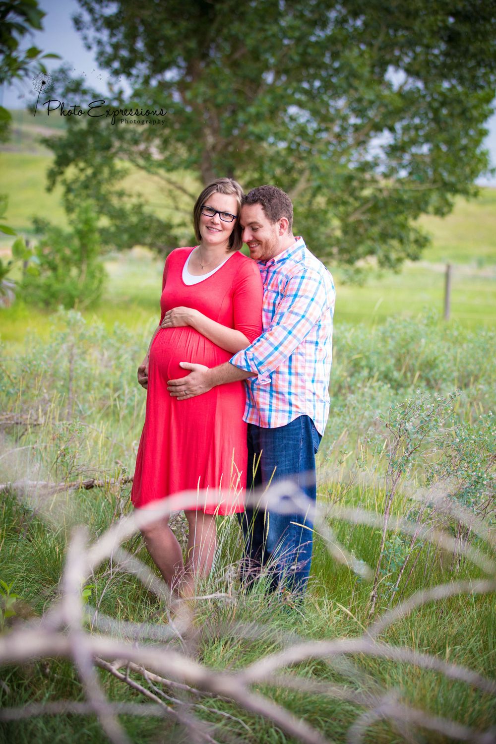Expectant couple shares intimate moment in rustic outdoor setting.