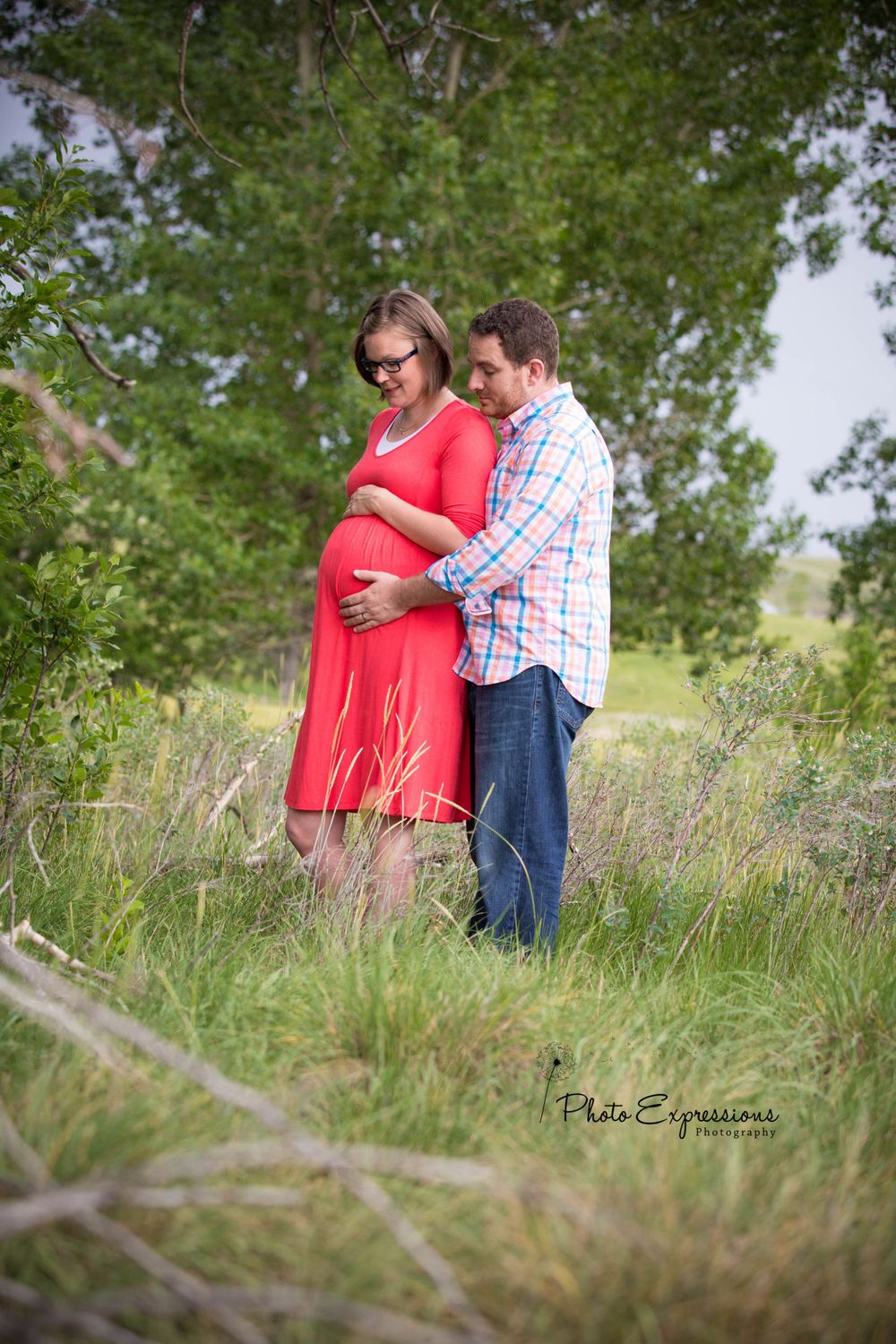 Couple poses in tall grass field during maternity photoshoot.