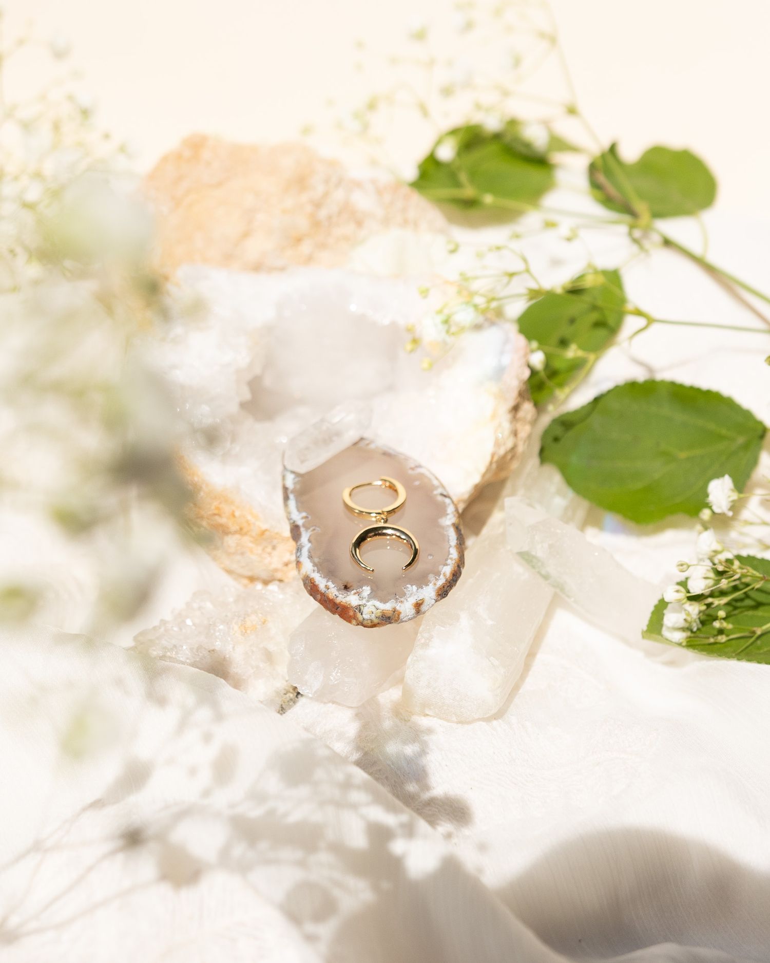 Gold wedding rings nestled in a delicate geode with green leaves and soft lighting.