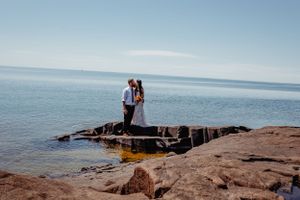 A couple shares an intimate moment on rocky shoreline overlooking calm lake waters.