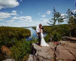 Two people share an intimate moment on a cliff edge with a stunning river valley vista.