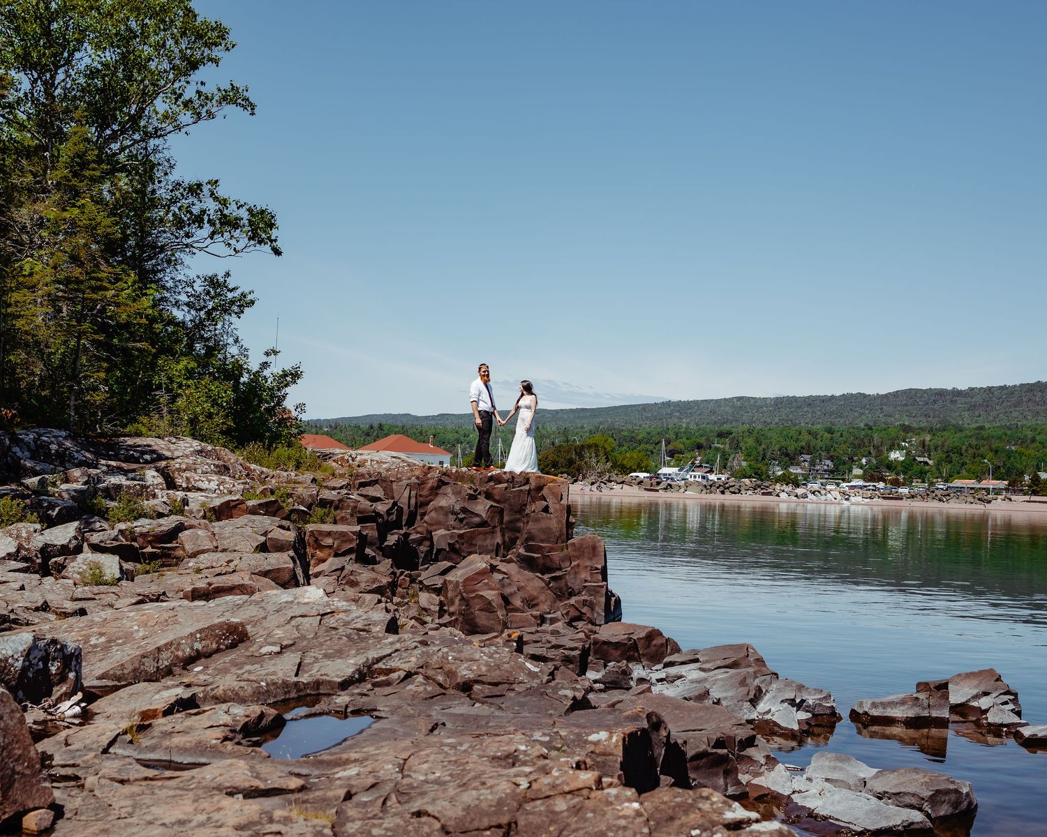 Joyful celebration pose on dramatic rocky cliff overlooking peaceful lake and distant shore.