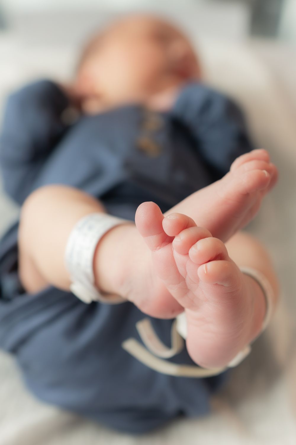 Newborn baby feet with hospital ID bracelet in soft focus, close-up photo of tiny infant toes.