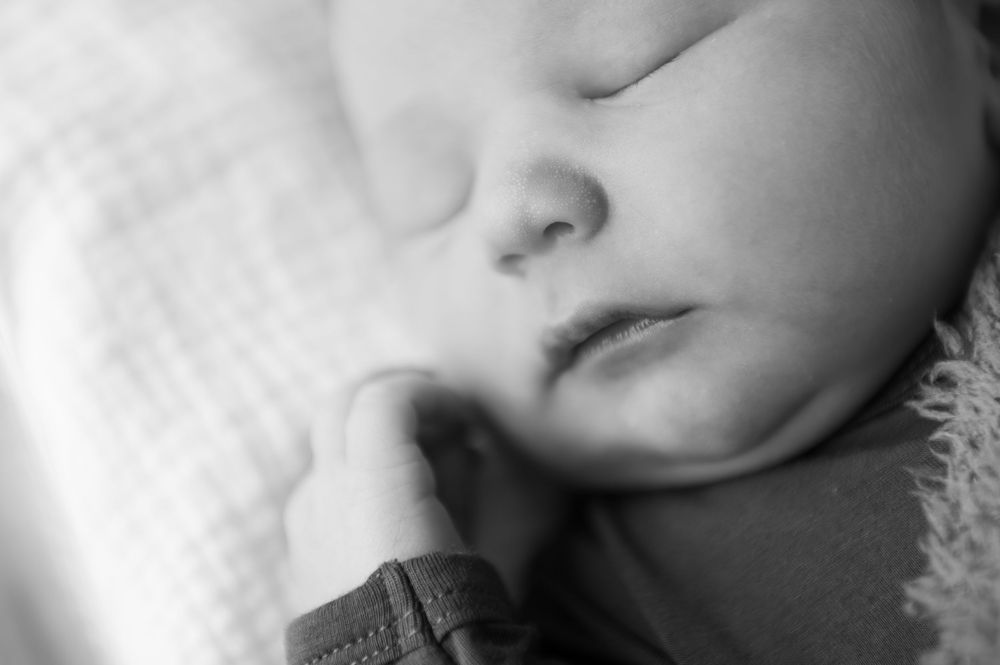 Black and white close-up photo of a peacefully sleeping newborn baby with tiny fingers near face.