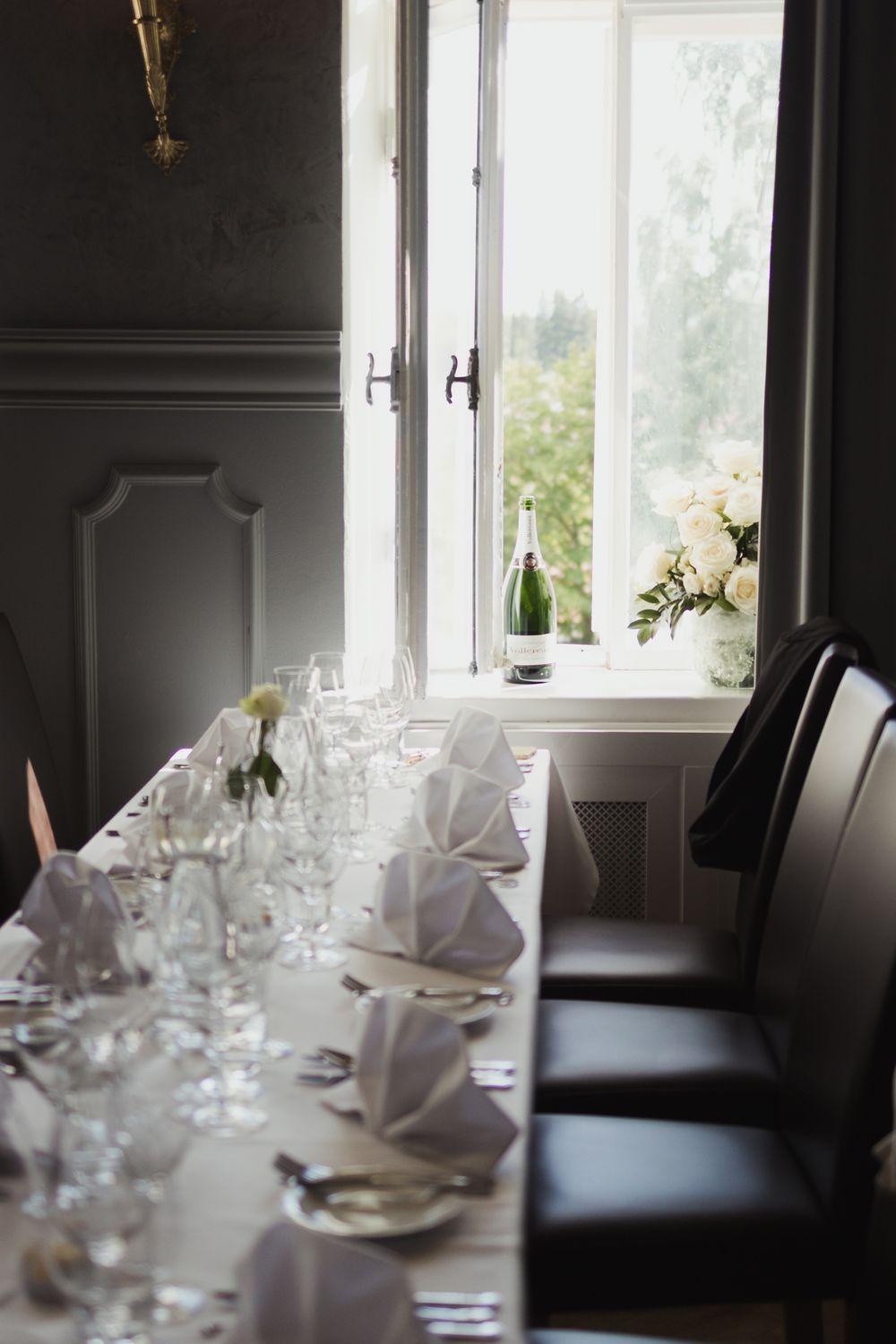 Elegant table setting with folded napkins, wine glasses and white flowers by a window.